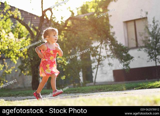 The playful cute little girl in dress is running on the street outdoors
