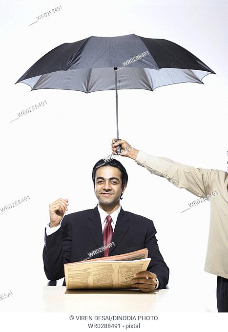 South Asian Indian executive holding newspaper sitting under umbrella MR702A