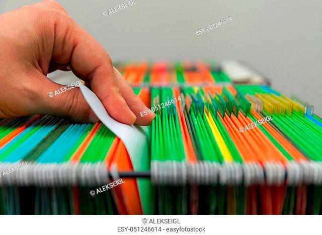 Abstract background of colorful hanging file folders in drawer. Mans hand. Stock photo