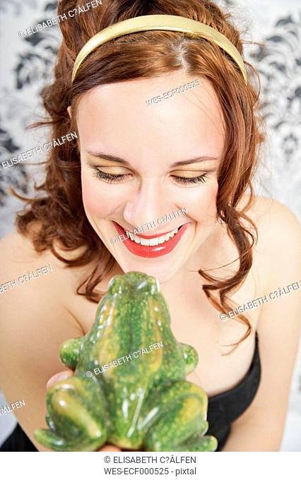 Portrait of smiling young woman kissing frog