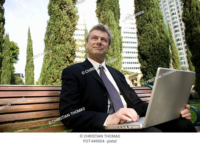 Businessman sitting on a park bench and using a laptop