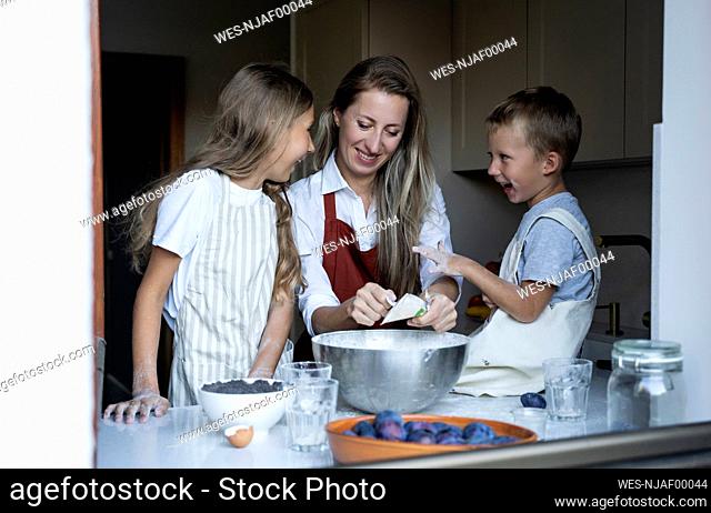 Cheerful children helping mother cooking at home