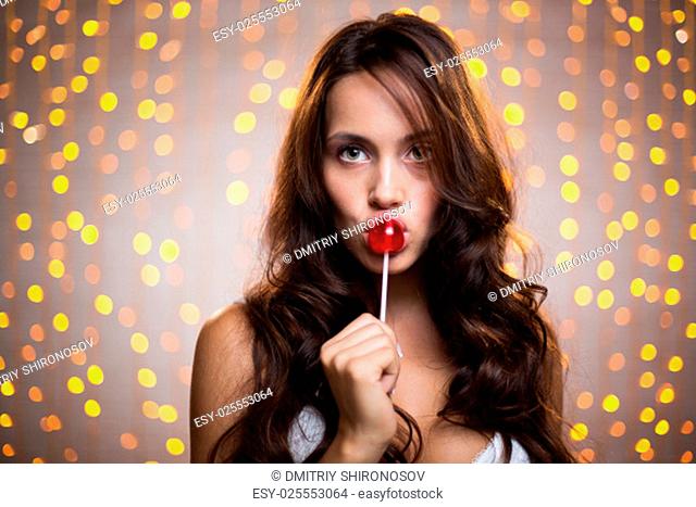 Pretty long-haired brunette with lollipop looking at camera on sparkling background