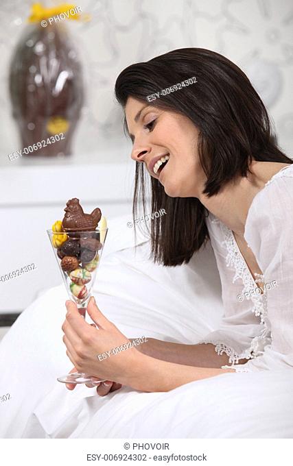 Woman lying in bed with a glass filled with chocolates
