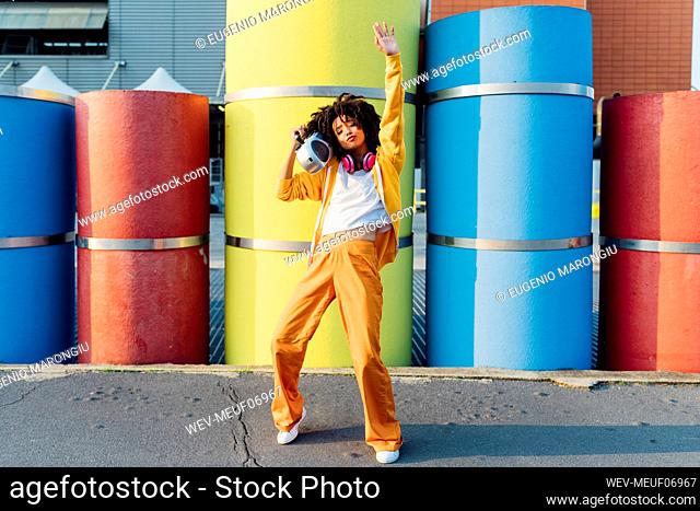 Young woman carrying boom box on shoulder dancing in front of colorful pipes