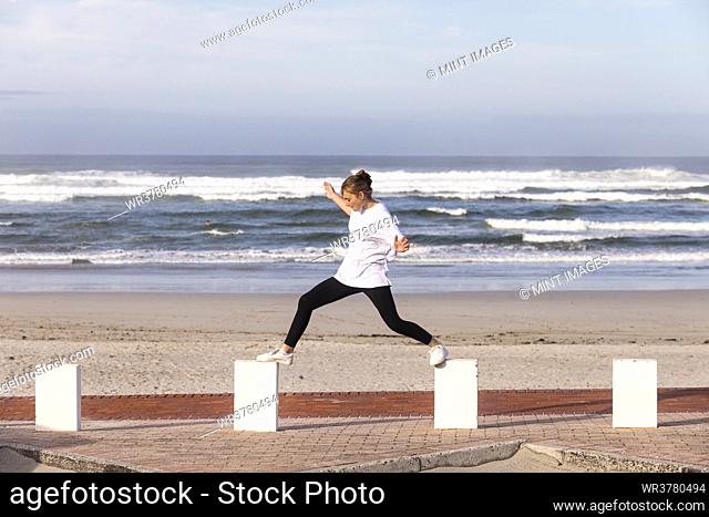 A teenage girl balancing on posts on a sandy beach