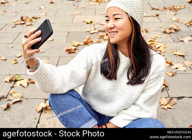 Smiling woman looking at video call on mobile phone while sitting on footpath