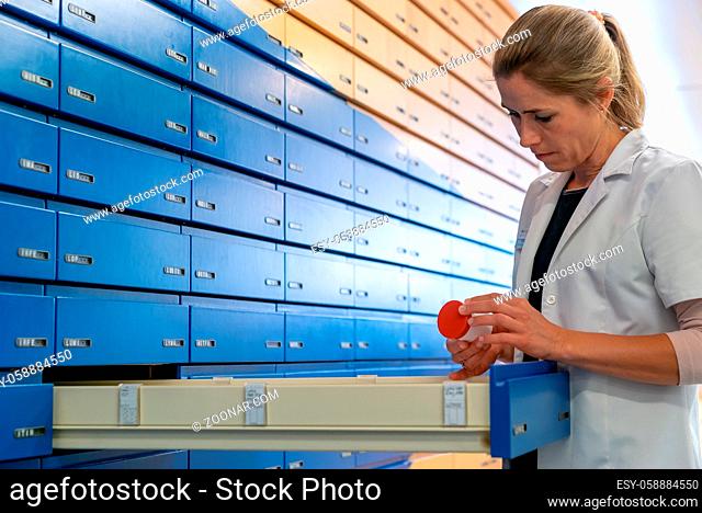 A blonde pharmacist checking a medical product and precription in one of the alphabetical pharmacy drawers