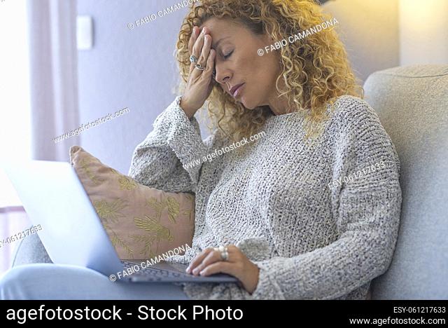 Sad tired young woman touching forehead having headache migraine or depression, frustrated adult female working on laptop computer sitting on the sofa at home