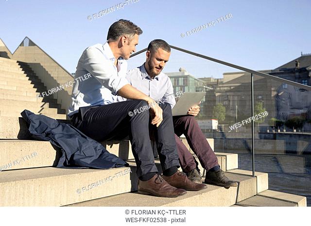 Two businessmen sitting on stairs using laptop