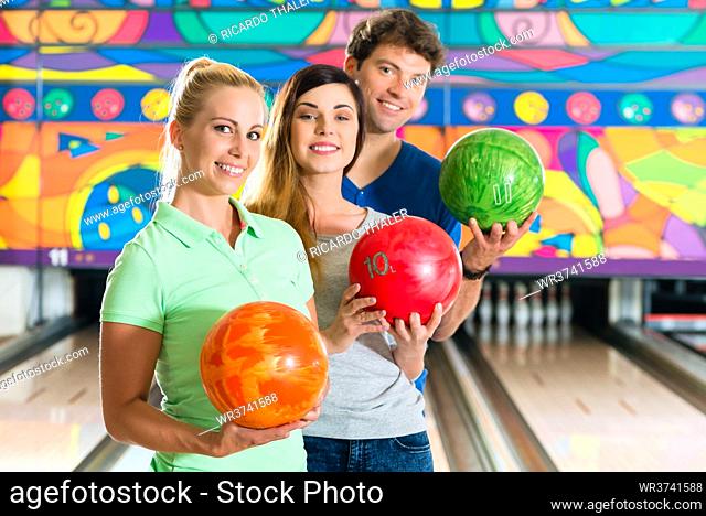 Young people or friends, man and women, playing bowling with a ball in front of the ten pin alley, they are a team