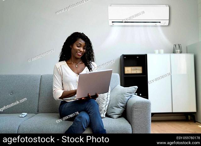 Young Happy Woman Sitting On Couch Using Air Conditioner At Home