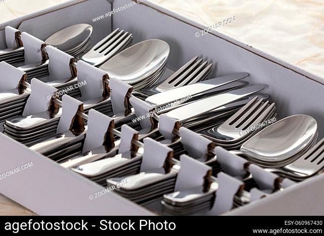 New from the store, spoons, forks, knives, cake forks and teaspoons in a box, on table with white tablecloth, twelve of each piece. Close view