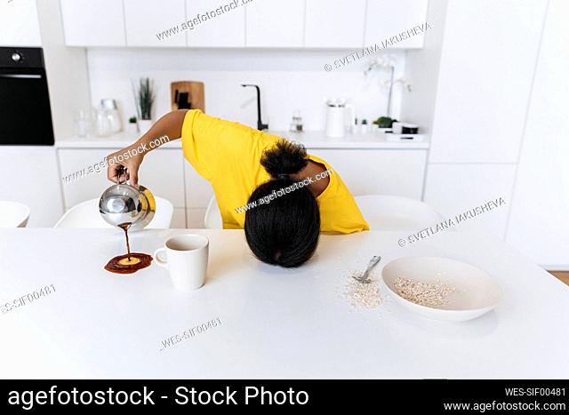 Exkausted woman spilling coffee on kitchen table