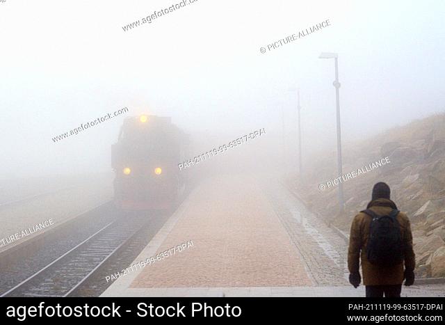 19 November 2021, Saxony-Anhalt, Brocken: The Brockenbahn of the Harzer Schmalspurbahnen (HSB) enters the station on the Brocken in dense fog