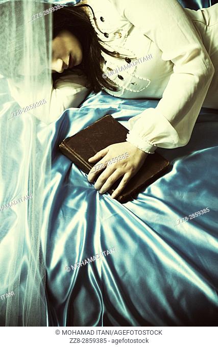 Sad young woman laying down in bed hand on book