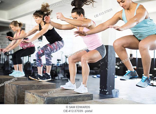 Determined women doing jump squats on boxes in exercise class