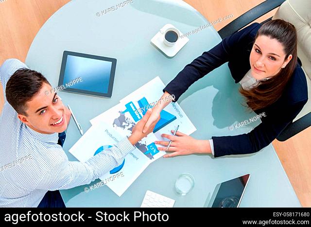 Top view of young Business partners closing a deal.Couple shaking hands over deal with documents and digital tablet on table showing statistics and graphics