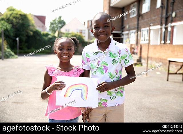Portrait cute brother and sister holding rainbow drawing outside