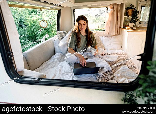 Young female freelancer using laptop on bed in camper