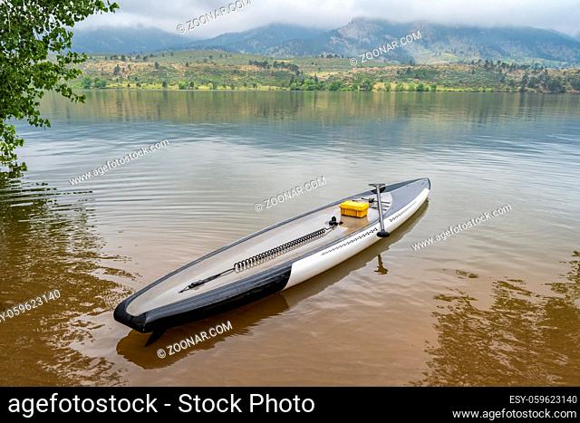 performance stand up paddleboard with a safety coil leash, paddle, and waterproof case on a calm mountain lake - Horsetooth Reservoir in northern Colorado
