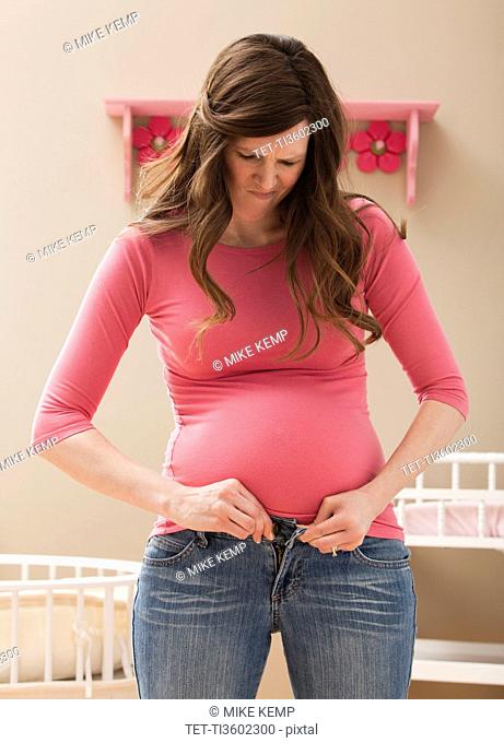 USA, Utah, Lehi, Young pregnant woman buttoning jeans