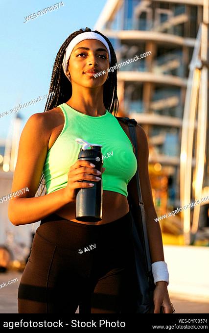 Young sportswoman looking away while holding water bottle