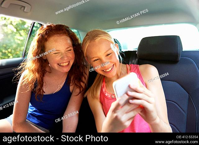 Happy preteen girl friends taking selfie in back seat of car