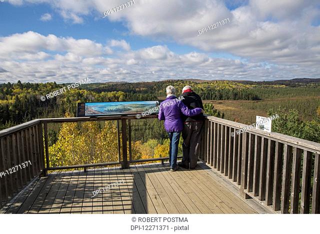 Mature couple overlooking Sunday Creek from the Algonquin Park visitor centre observation deck on a sunny afternoon in autumn; Ontario, Canada