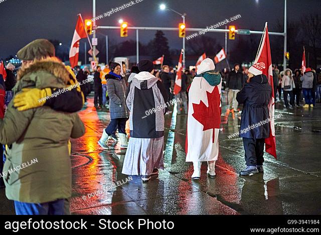 People wear and hold the Canadian flag at an intersection on 11 February 2022, day five, of the Freedom convoy blockade in Windsor