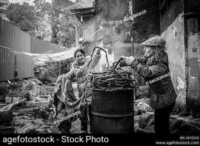 Street scene in an old town quarter of Chongqing. Women are smoking homemade sausages. These districts are gradually being demolished to make room for new...