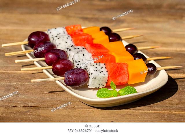 Fresh tropical fruit - grapes, mango, watermelon and pitahaya on skewers in white plate - healthy breakfast, weight loss concept. Thailand. Close up