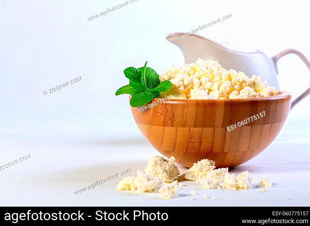 Homemade cottage cheese is served in a wooden bowl and with jug of fresh sour cream. Concept of healthy eating