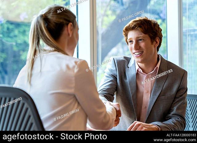 Young man shaking hands with mature woman in office