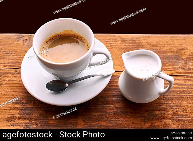 Coffee with milk in ceramic cup with small milk jug
