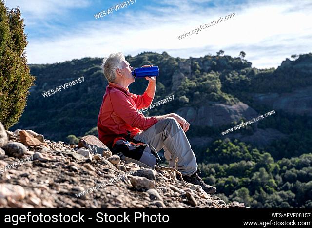 Male hiker drinking water while sitting on mountain at Sant Llorenc del Munt i l'Obac, Catalonia, Spain
