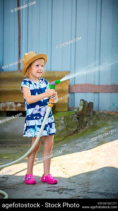 Little girl in hat watering lawn. Summer day