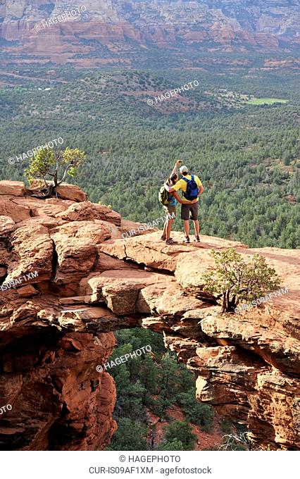 Hiking couple viewing from arched rock formation, Sedona, Arizona, USA