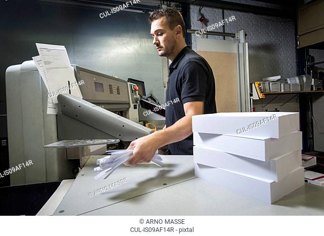 Worker disposing of paper trimmings in print workshop