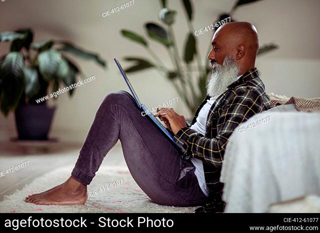 Mature man with beard using laptop on floor