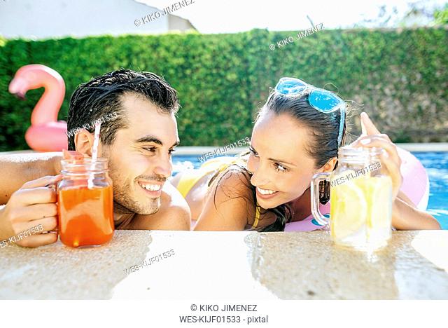 Happy couple in swimming pool with drinks at the poolside