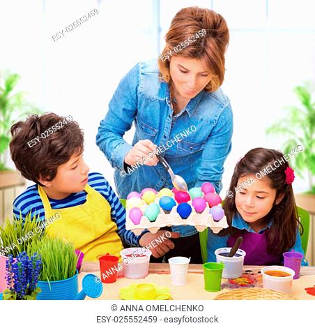 Happy family paint Easter eggs at home, mother showing her precious kids how to make traditional Easter decorative food