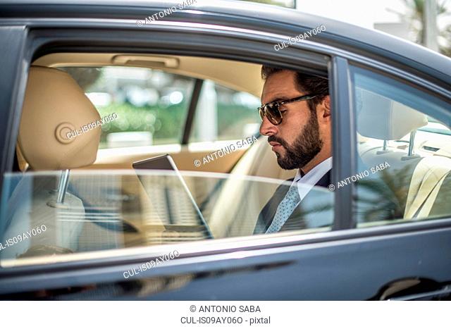 Young businessman using digital tablet in car backseat, Dubai, United Arab Emirates