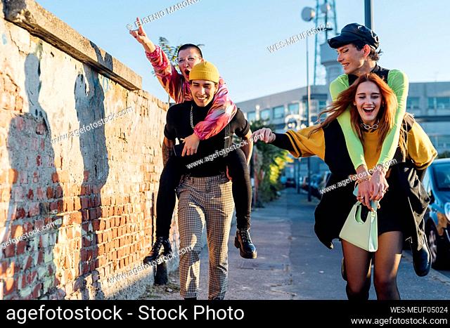 Cheerful man and woman piggybacking friends on footpath