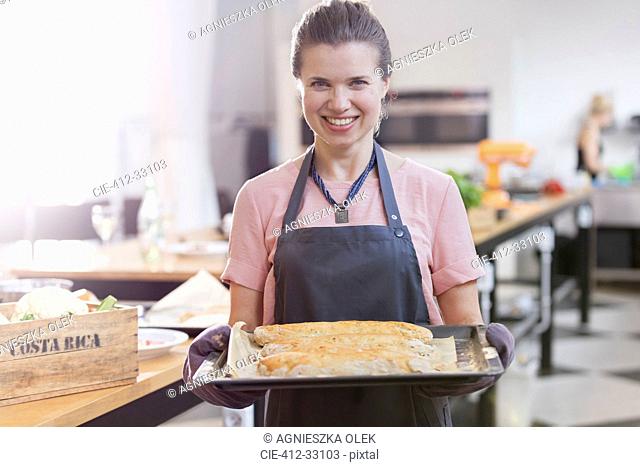 Portrait smiling woman holding tray of food in cooking class kitchen