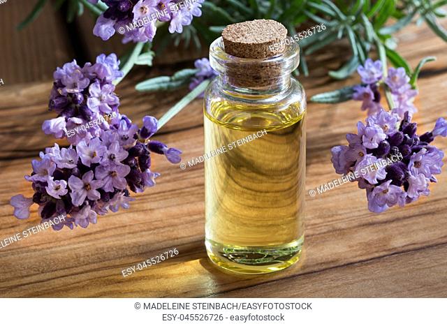 A bottle of lavender essential oil with fresh lavender twigs on a wooden background