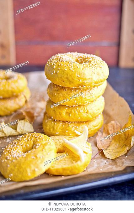 A stack of pumpkin bagels with autumnal leaves on a baking tray
