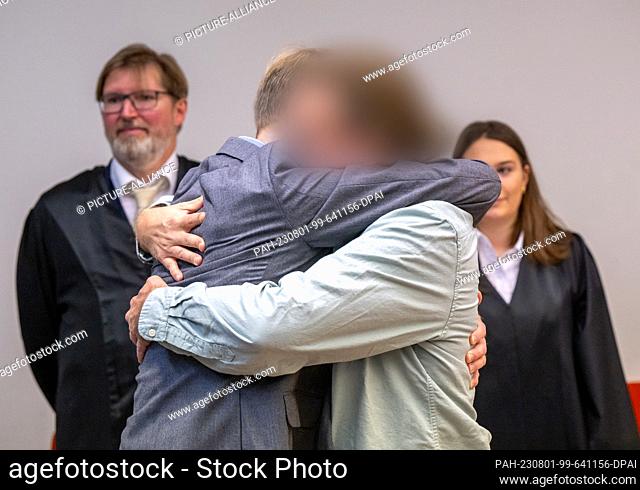 01 August 2023, Bavaria, Munich: The defendant (center right) stands in the courtroom in front of his two lawyers and is embraced by his brother (center left)