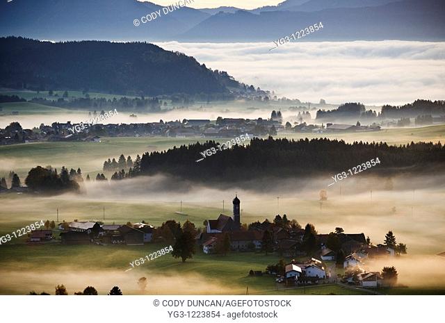 Autumn morning fog clears from village of Speiden and rural landscape of Allgaeu region, near Eisenberg, Bavaria, Germany
