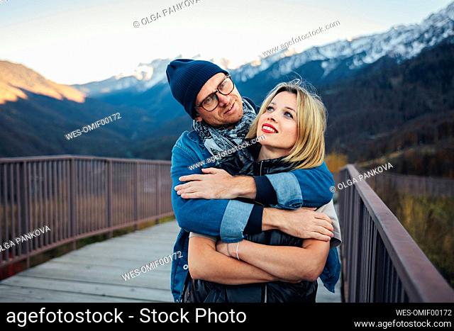 Man hugging woman from behind on bridge